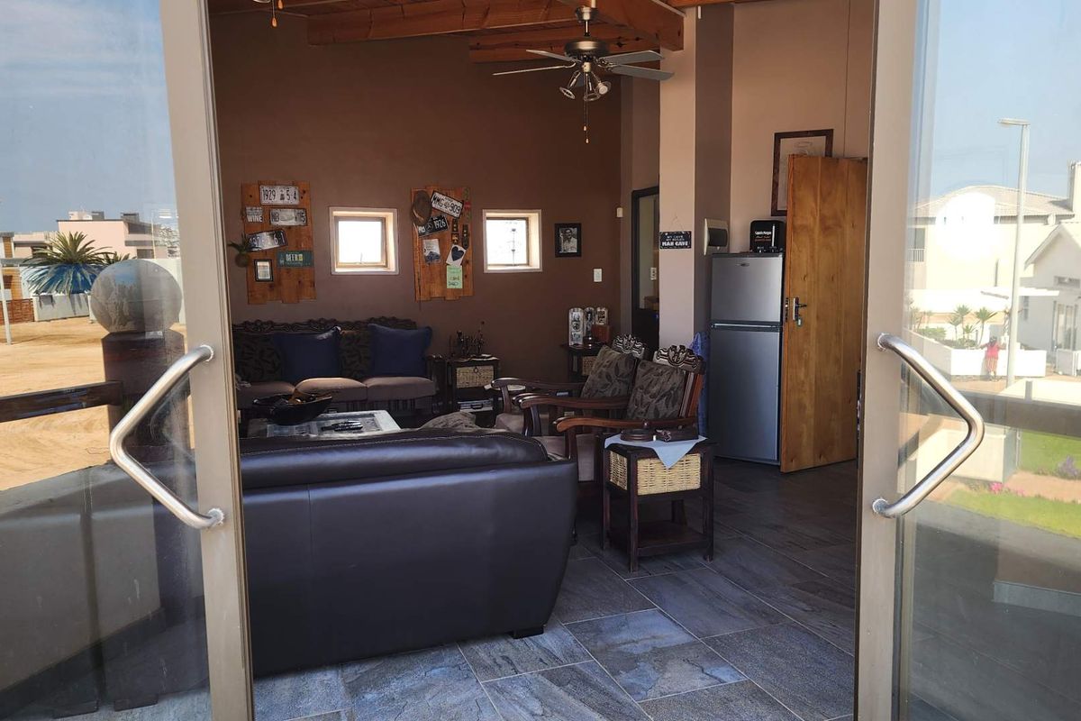 A living room featuring exposed timber ceiling beams, a ceiling fan, and tiled flooring, accessible through large sliding glass doors.