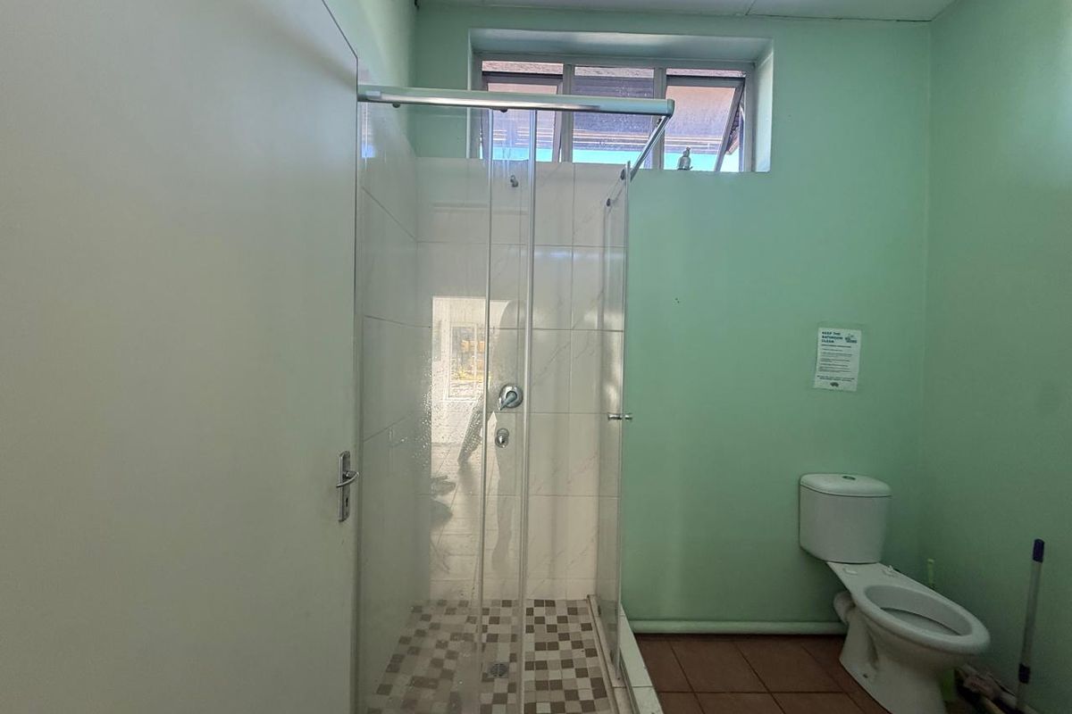 A functional office bathroom featuring a glass-enclosed shower, ceramic toilet, and tiled flooring, requiring cosmetic updates to improve its overall condition.