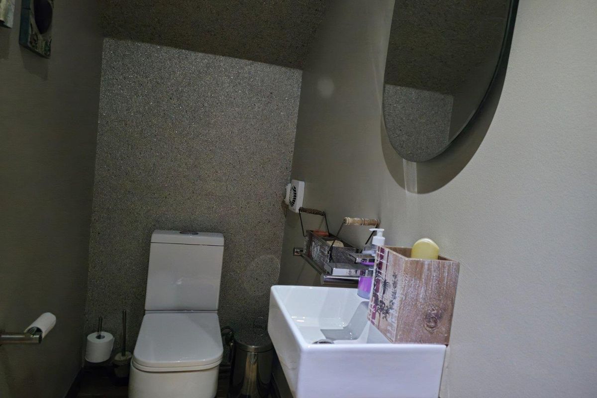 A compact guest bathroom featuring a modern wall-mounted basin, a standard toilet, and a textured feature wall.