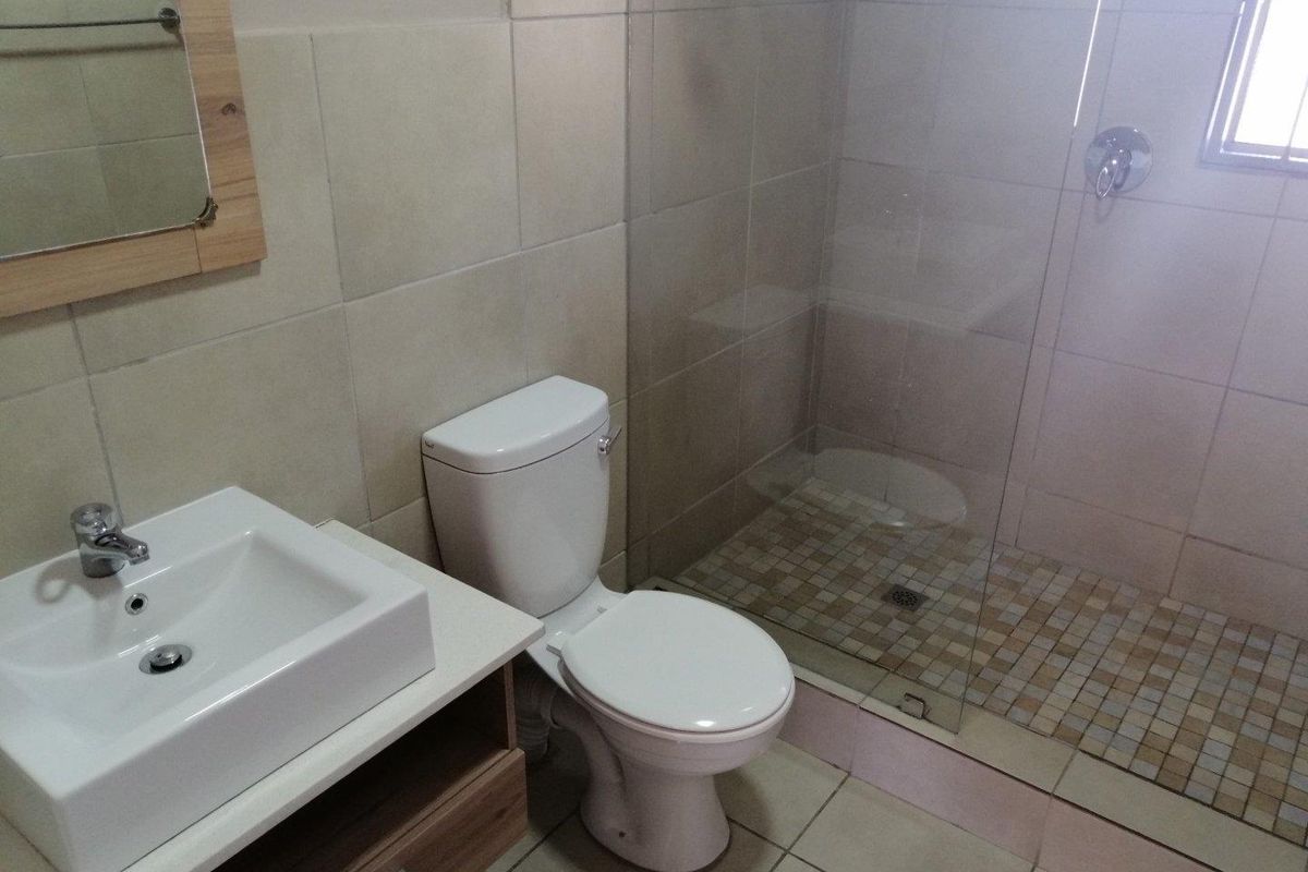 A clean, modern bathroom featuring a vanity basin, toilet, and a glass-enclosed walk-in shower with neutral wall and floor tiling.