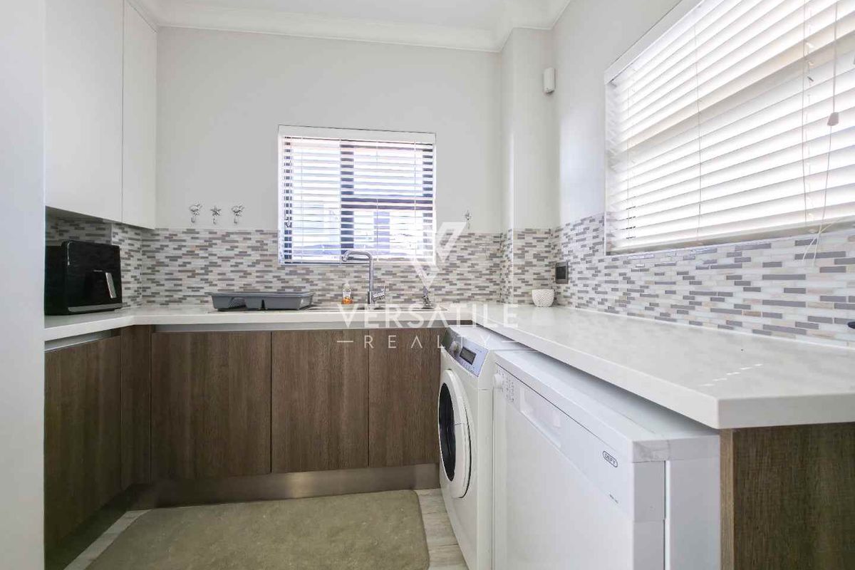 A functional kitchen featuring modern cabinetry, stone countertops, a mosaic tile backsplash, and integrated space for laundry appliances.