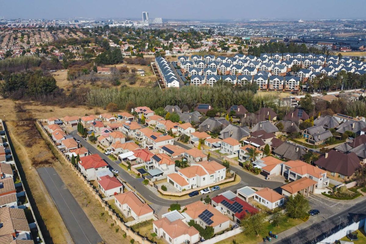 An aerial view of a residential estate featuring multiple detached houses with tiled roofs, solar panels, and established road infrastructure.