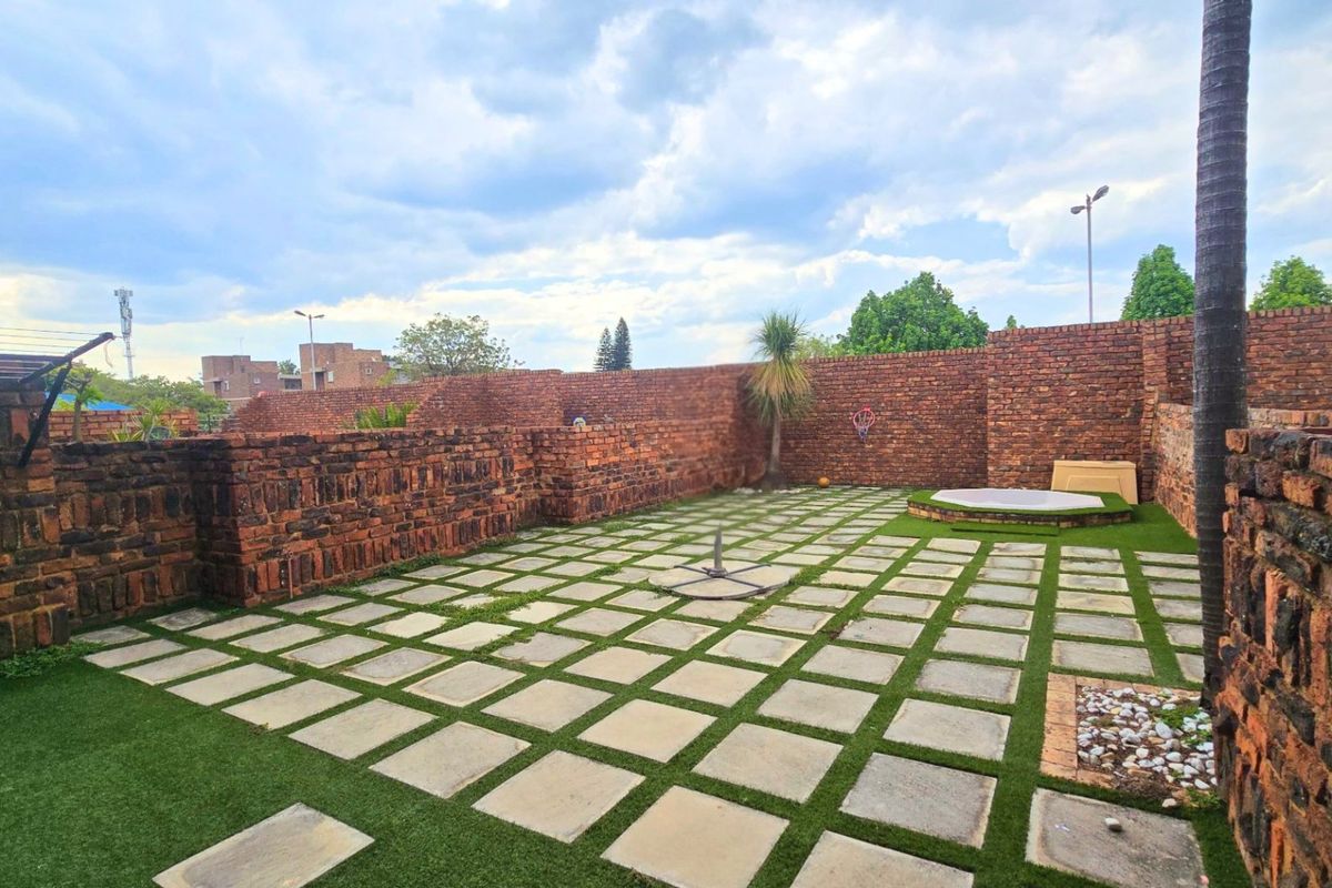 A spacious rear courtyard featuring brick boundary walls, paved flooring, and artificial turf, offering a private outdoor area for relaxation or entertainment.