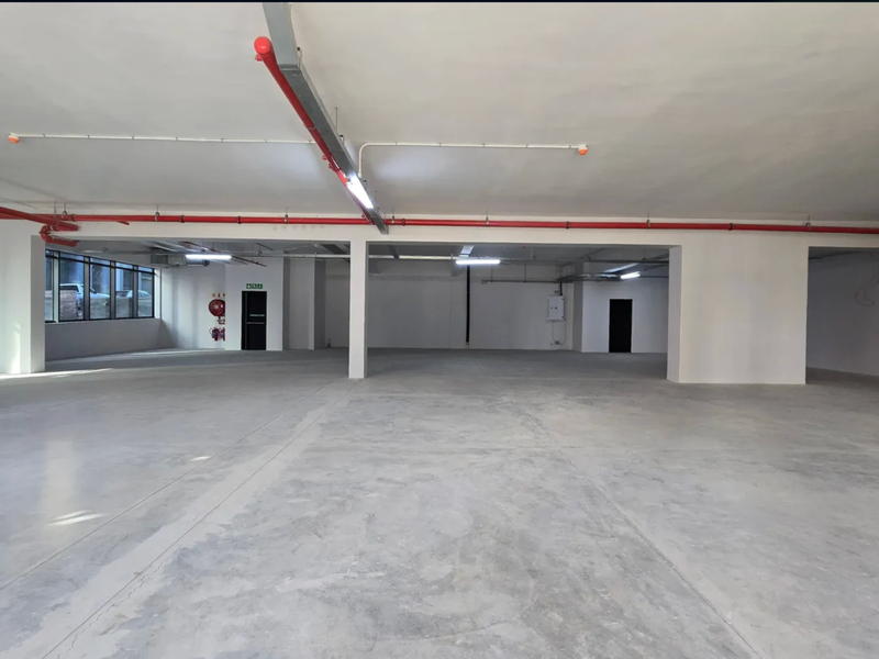 A spacious, open-plan commercial retail unit featuring polished concrete floors, exposed fire suppression systems, and ample natural light from large windows.