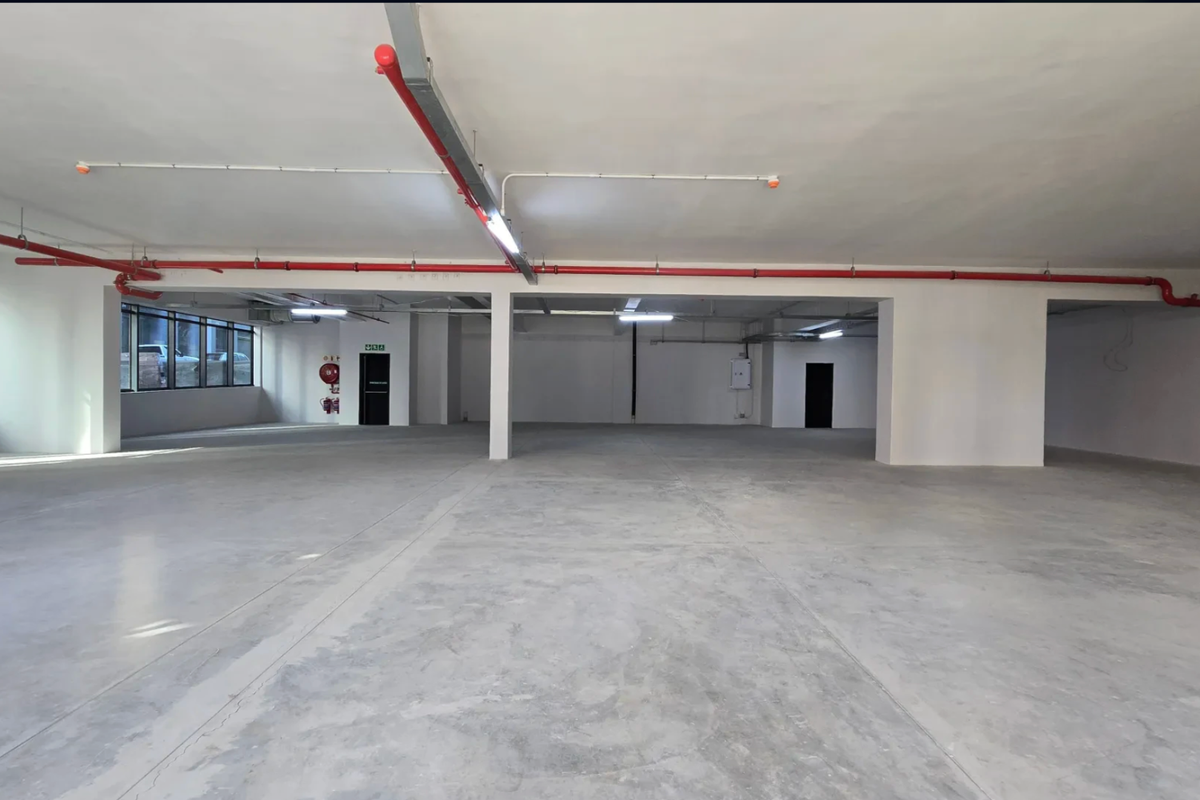 A spacious, open-plan commercial retail unit featuring polished concrete floors, exposed fire suppression systems, and ample natural light from large windows.