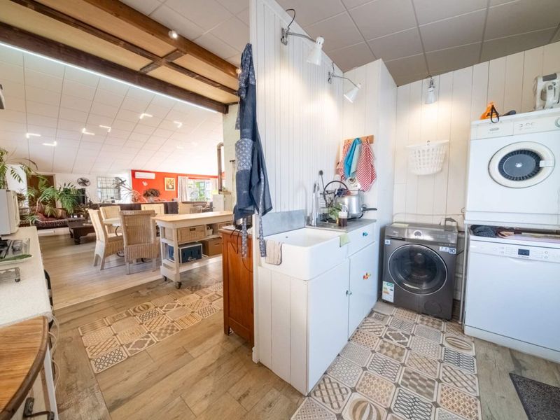 A functional laundry area featuring a farmhouse sink, built-in cabinetry, and patterned tiled flooring, seamlessly connected to the adjacent open-plan living space.