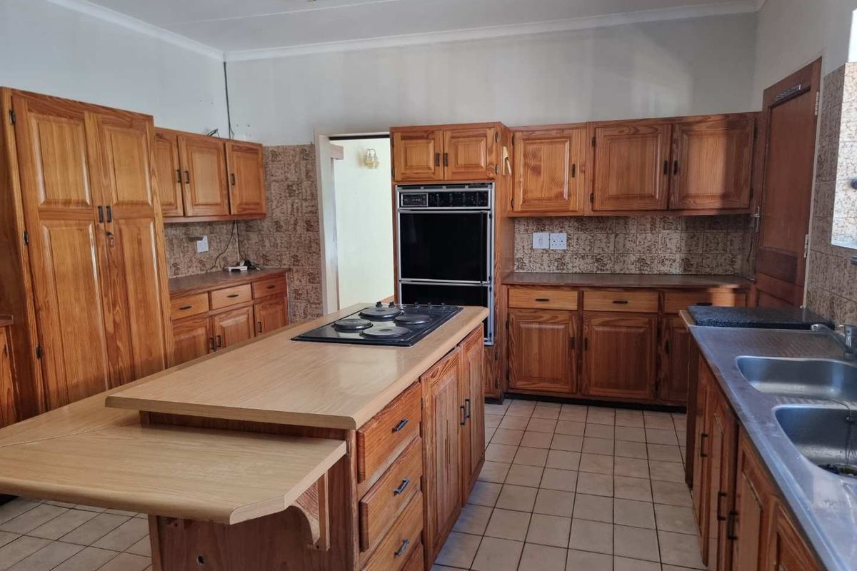 Spacious kitchen featuring extensive timber cabinetry, a central island with a built-in hob, double wall oven, and double stainless steel sink.