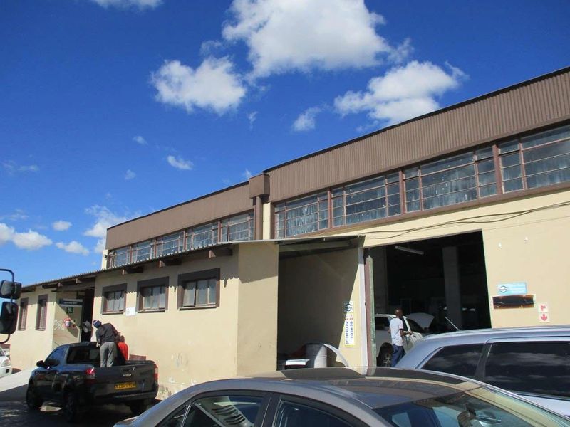 Exterior view of an industrial warehouse facility featuring a large roller shutter entrance, clerestory windows, and a corrugated metal roof structure.