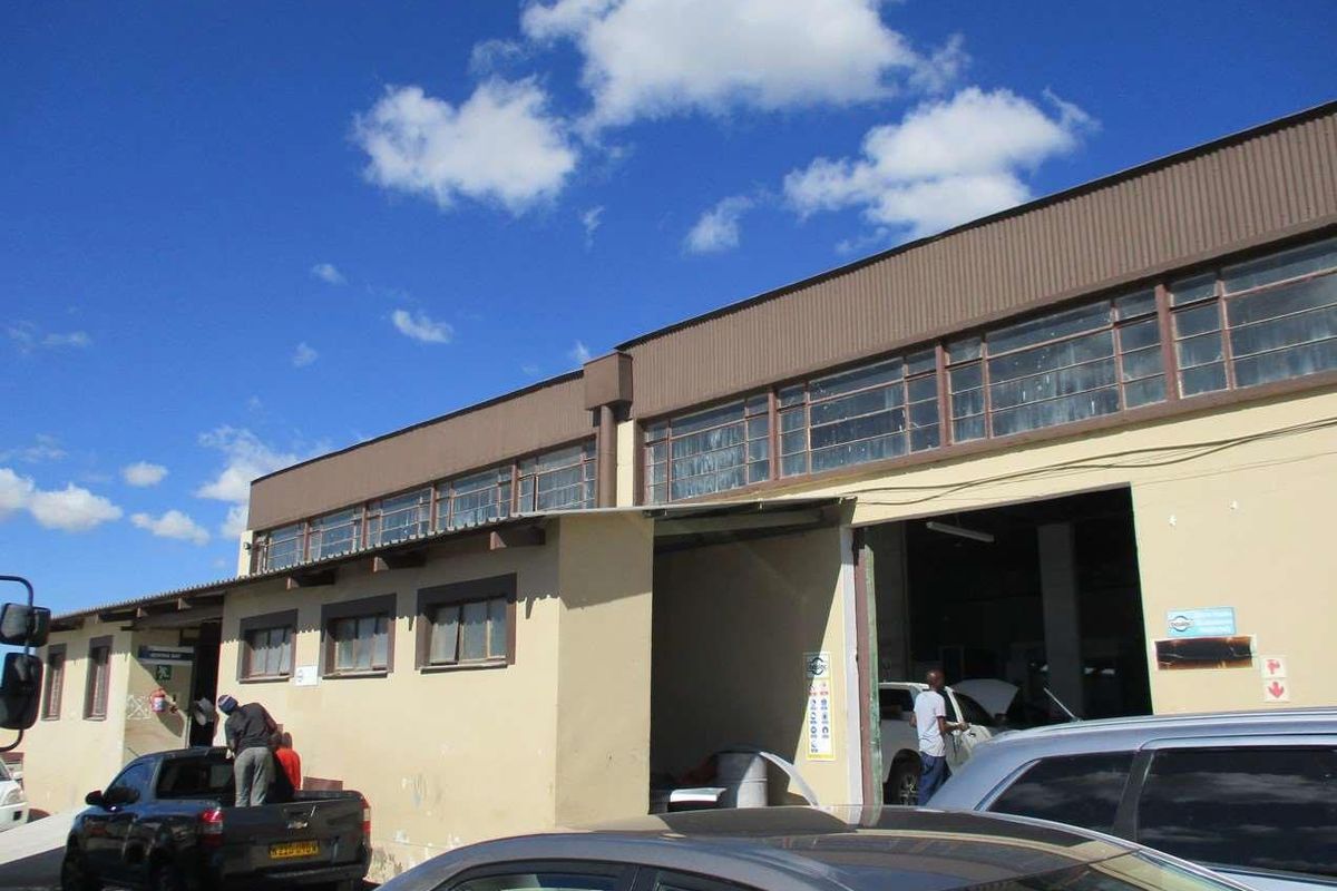 Exterior view of an industrial warehouse facility featuring a large roller shutter entrance, clerestory windows, and a corrugated metal roof structure.