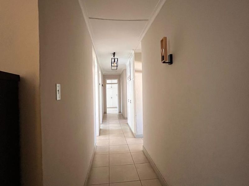 A clean, well-lit hallway featuring neutral tiled flooring, built-in storage cupboards, and modern wall-mounted lighting fixtures.