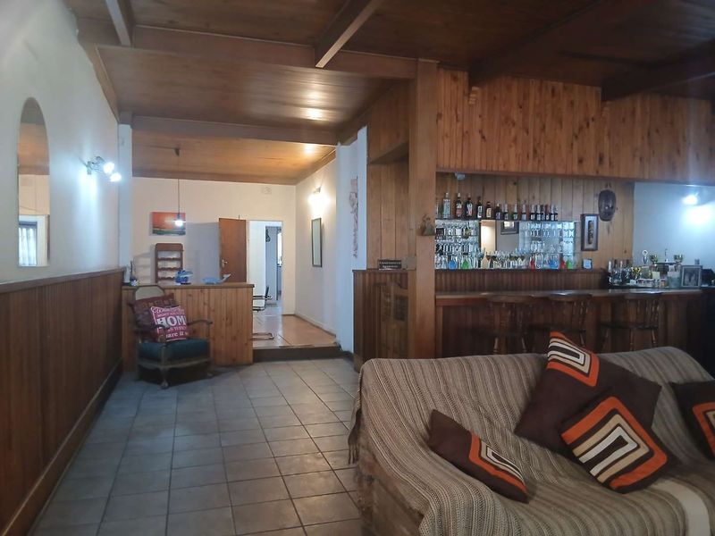 A spacious living area featuring a built-in bar with timber paneling, exposed timber ceiling beams, and tiled flooring throughout.