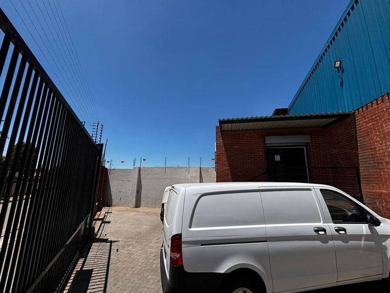 Rear exterior view of a commercial property featuring brick and metal cladding, paved driveway, and secure perimeter electric fencing.