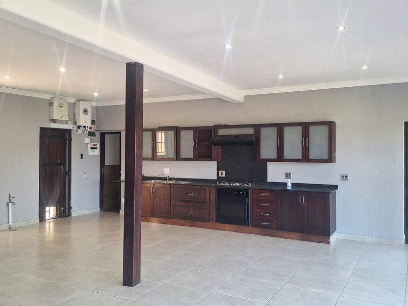 Spacious open-plan living and kitchen area featuring dark wood cabinetry, granite countertops, built-in appliances, tiled flooring, and recessed lighting.