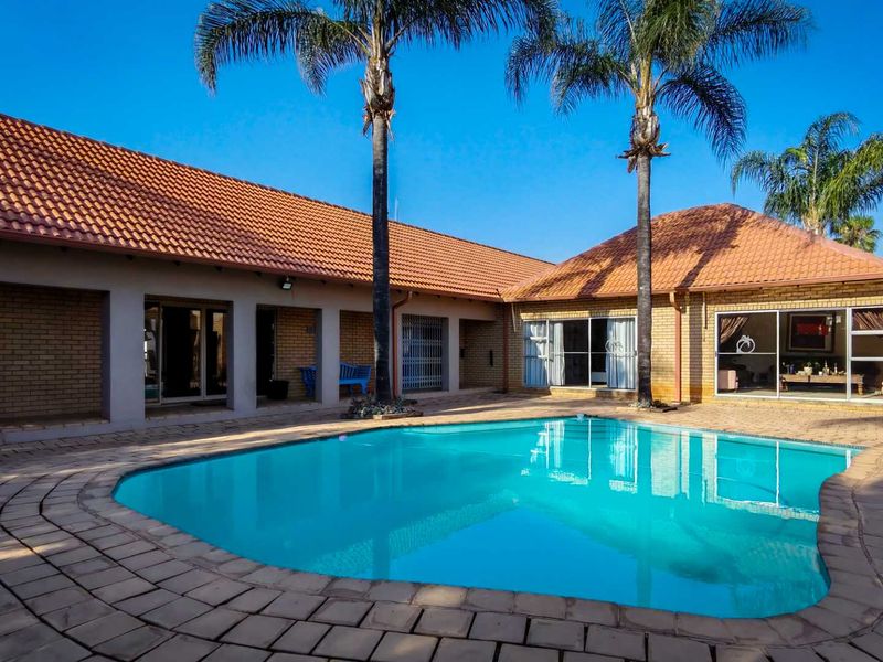 A well-maintained outdoor pool area featuring a paved deck, brick exterior walls, and a tiled roof, providing a pleasant space for relaxation.