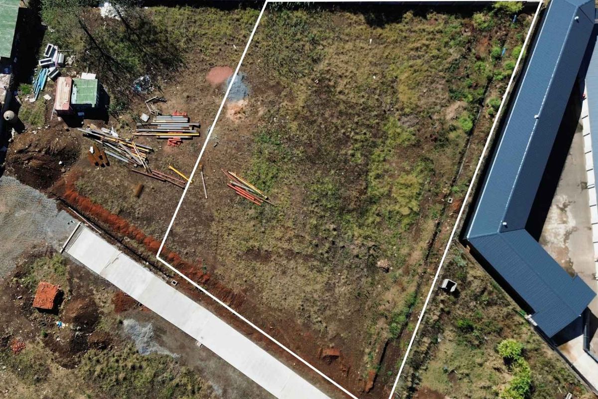 Aerial view of a vacant commercial land plot featuring defined boundaries, concrete access, and surrounding perimeter fencing.