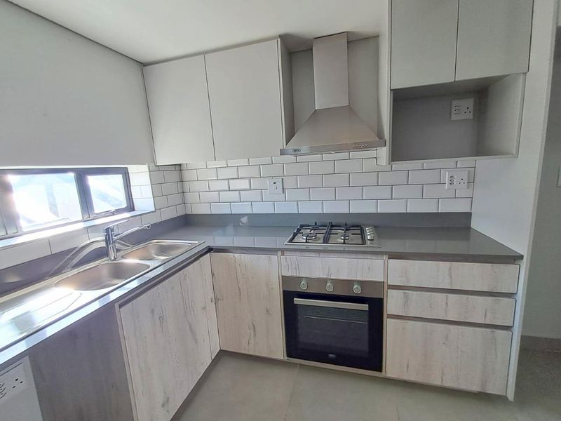 Modern kitchen featuring light wood-grain cabinetry, stone countertops, subway tile backsplash, and integrated stainless steel appliances including a gas hob and oven.