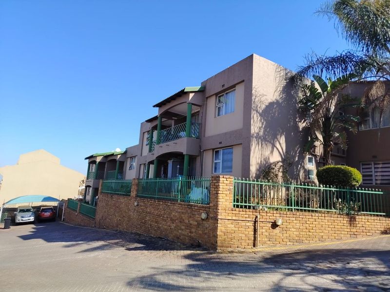 Exterior view of a multi-story townhouse complex featuring brick boundary walls, metal security fencing, and private balconies.
