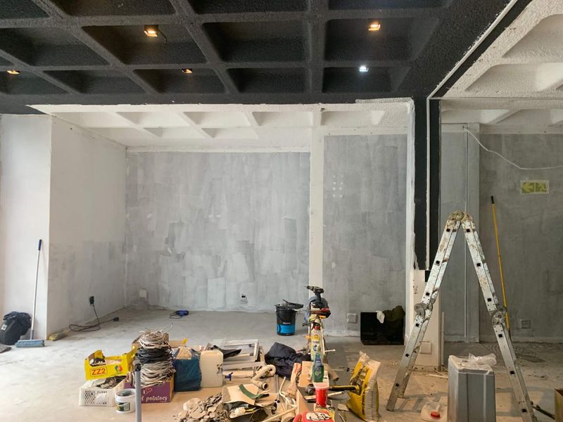 An open-plan retail space currently undergoing renovation, featuring a distinctive black coffered ceiling with recessed lighting and unfinished wall surfaces.