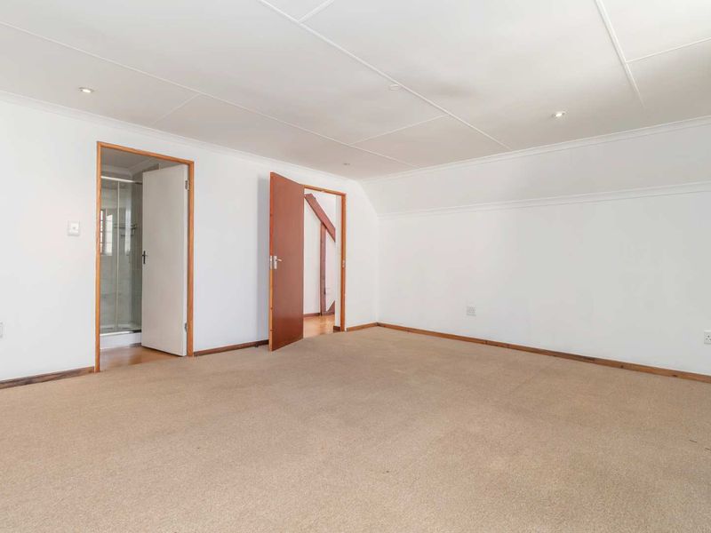 A spacious, empty bedroom featuring neutral carpeting, recessed lighting, and direct access to an en-suite bathroom.