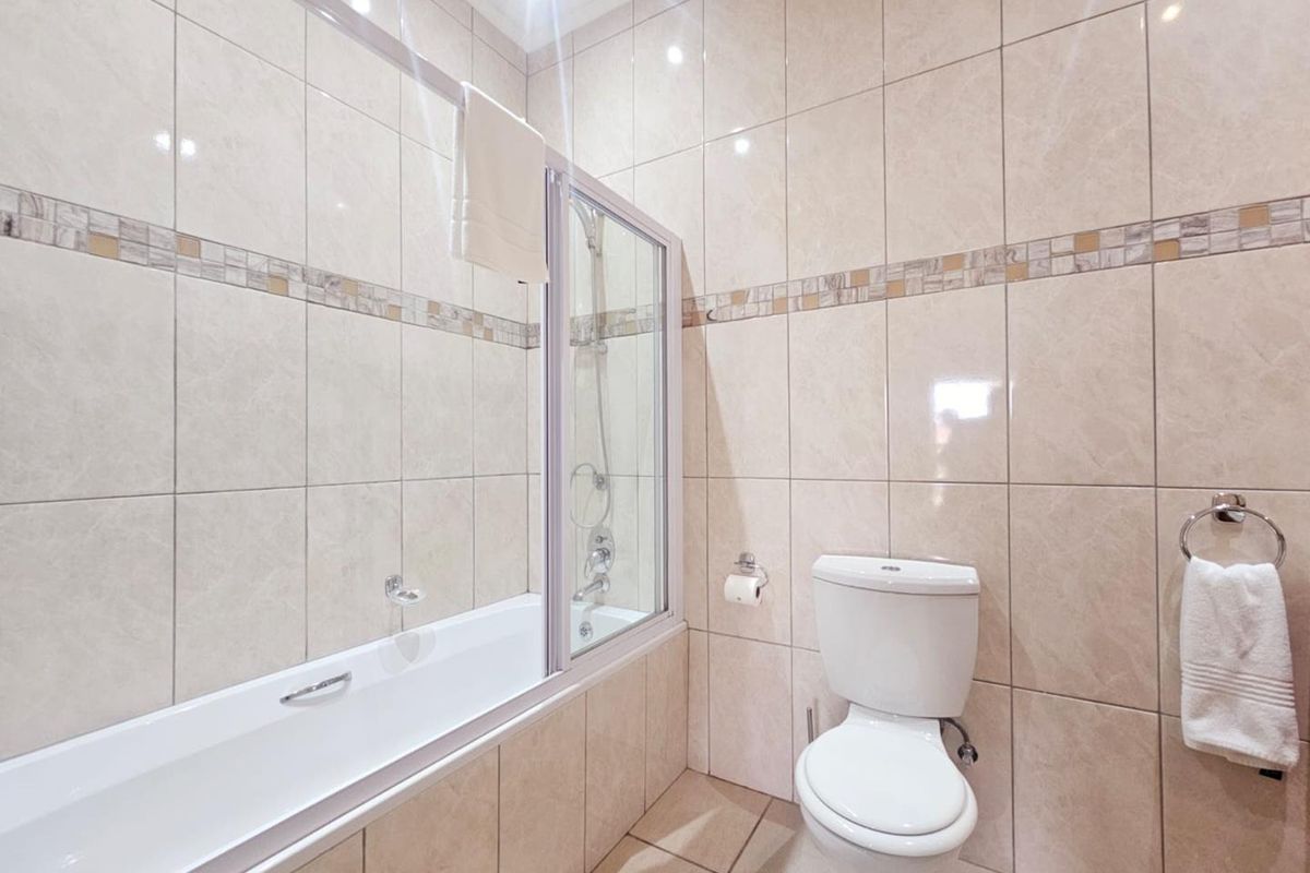 A clean, tiled bathroom featuring a built-in bathtub with a glass shower screen and a standard toilet.