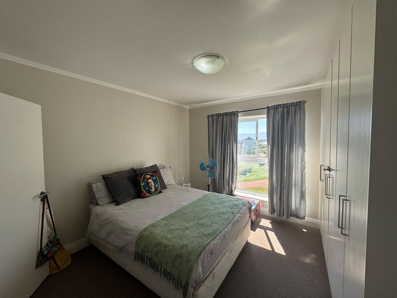 A well-lit bedroom featuring neutral walls, carpeted flooring, and ample built-in cupboard storage with a view of the surrounding area.