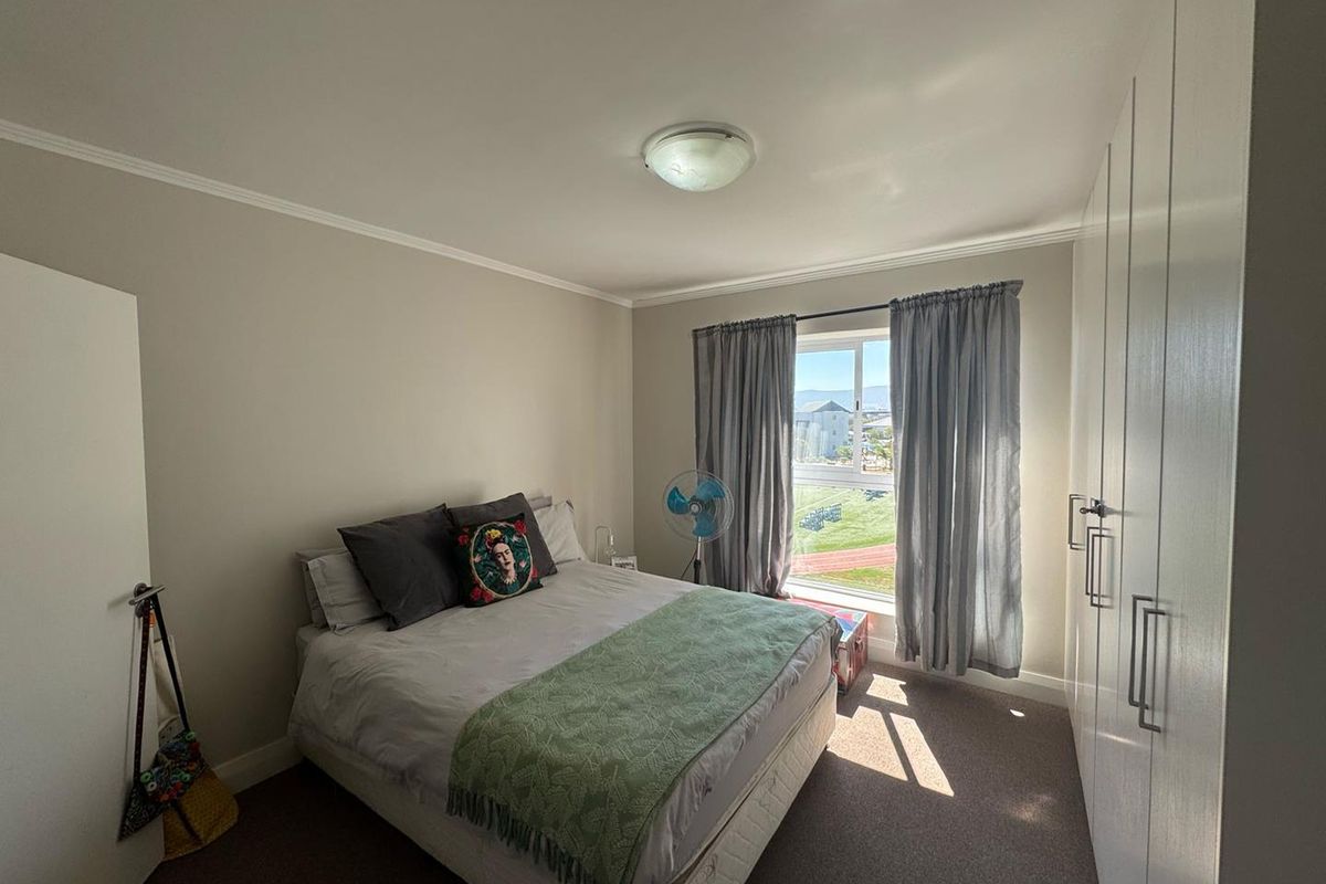 A well-lit bedroom featuring neutral walls, carpeted flooring, and ample built-in cupboard storage with a view of the surrounding area.