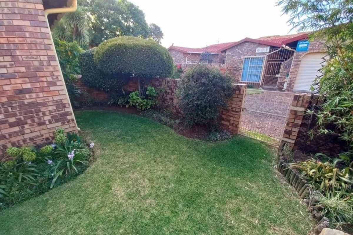 A well-maintained rear garden area featuring a manicured lawn, established shrubs, face brick boundary walls, and a secure metal gate leading to the driveway.