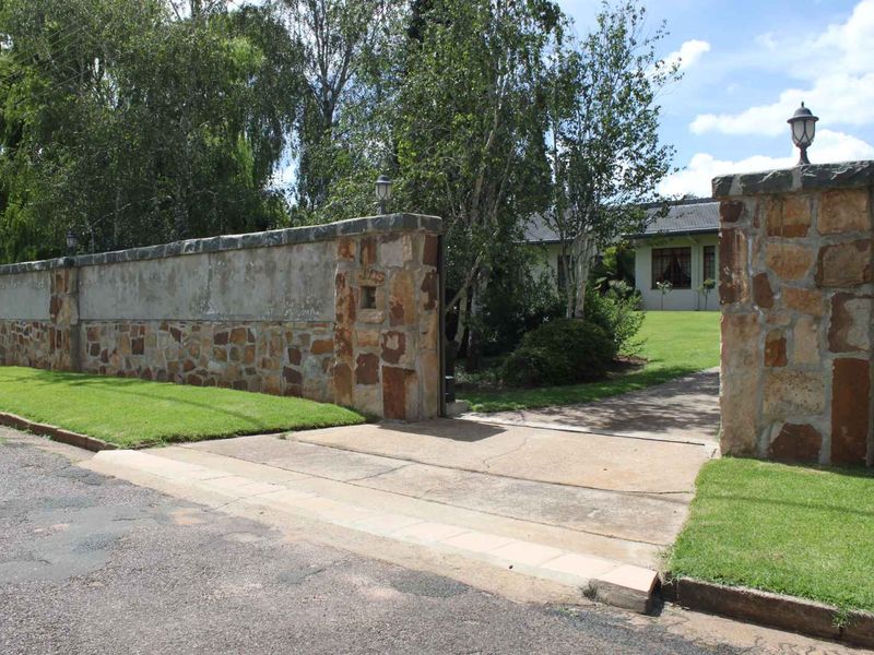 Front entrance view of the cottage featuring a stone boundary wall, concrete driveway, and established garden landscaping.