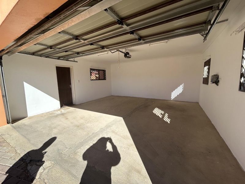 A spacious, empty double garage featuring concrete flooring, an automated door mechanism, and security-barred windows for added protection.