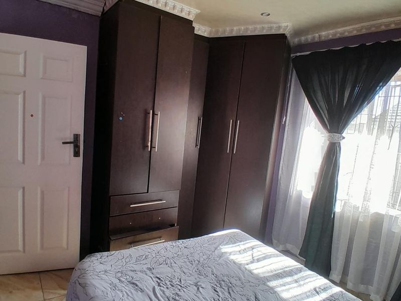 A bedroom featuring dark built-in cupboards, crown molding, and tiled flooring, offering functional storage space with potential for cosmetic updates.