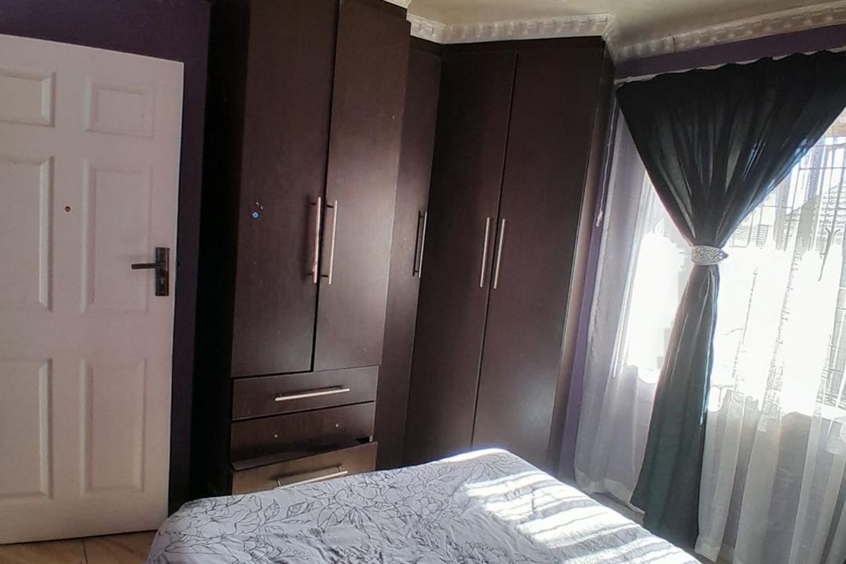A bedroom featuring dark built-in cupboards, crown molding, and tiled flooring, offering functional storage space with potential for cosmetic updates.