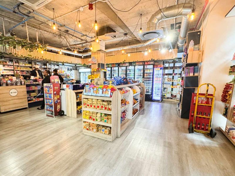 A well-lit retail space featuring an industrial-style exposed ceiling, commercial refrigeration units, and functional built-in shelving throughout the open-plan floor area.