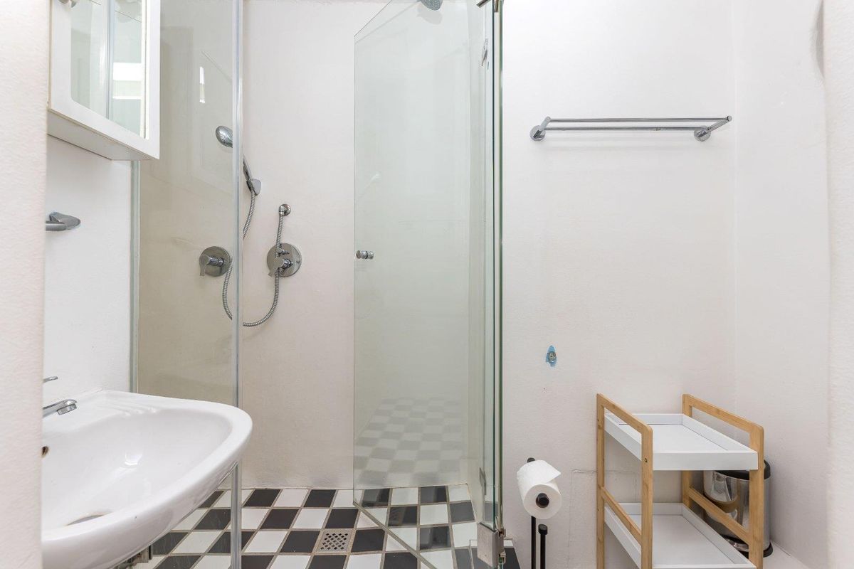 A functional bathroom featuring a glass shower enclosure, pedestal sink, and classic black and white checkered floor tiling.