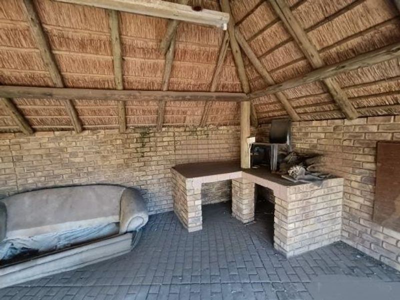 Outdoor entertainment area featuring a traditional thatch roof, exposed timber rafters, and a built-in brick braai station with paved flooring.