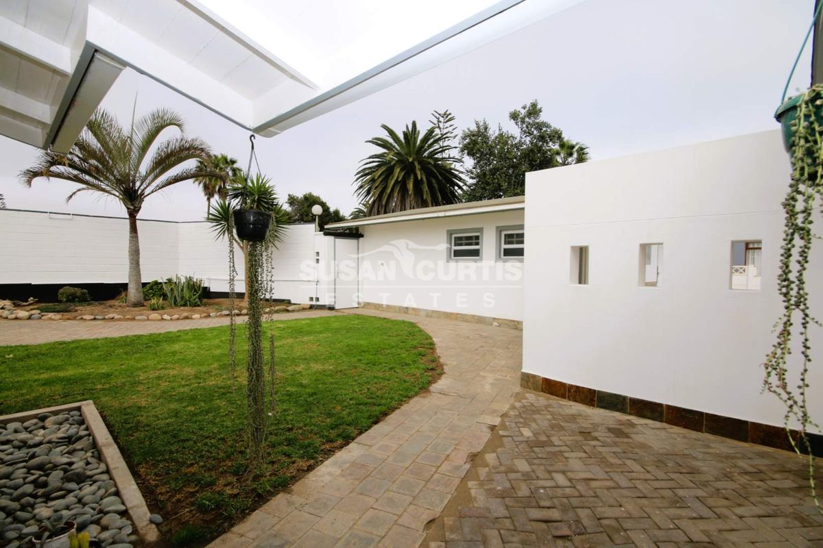 A well-maintained rear garden area featuring a paved walkway, manicured lawn, and a covered patio structure with clean white boundary walls.