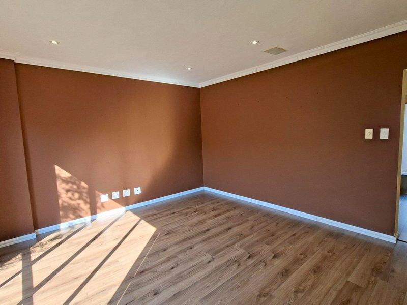 An empty living room featuring warm-toned walls, laminate flooring, and recessed downlighting, offering a clean and versatile space for interior design.