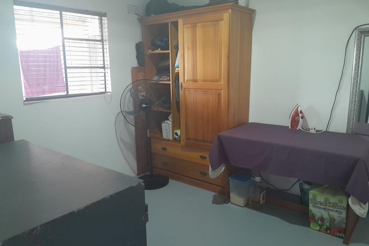 A bedroom featuring a window with security bars and a wall-mounted air conditioning unit.