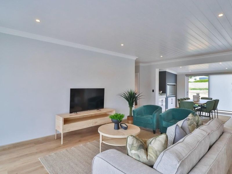 Bright open-plan living and dining area featuring timber-look flooring, recessed downlights, and a tongue and groove ceiling with seamless access to the outdoors.