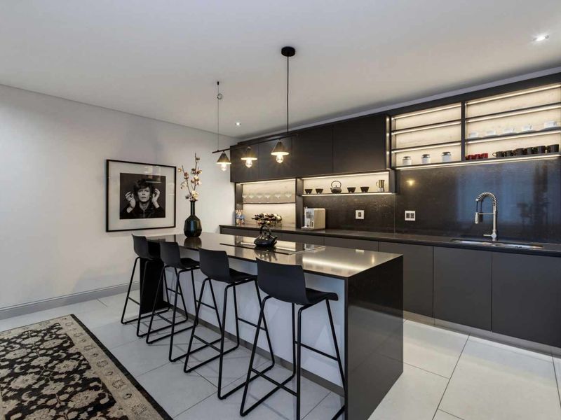 Modern kitchen featuring sleek dark cabinetry, stone countertops, a central island with breakfast bar seating, and integrated under-cabinet lighting.