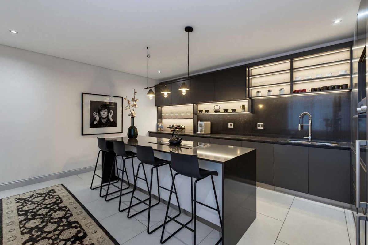 Modern kitchen featuring sleek dark cabinetry, stone countertops, a central island with breakfast bar seating, and integrated under-cabinet lighting.