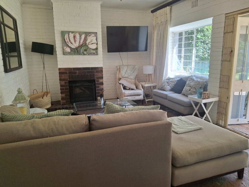Cozy living room featuring a classic brick fireplace, white painted brick walls, and large steel-framed windows providing natural light and garden views.