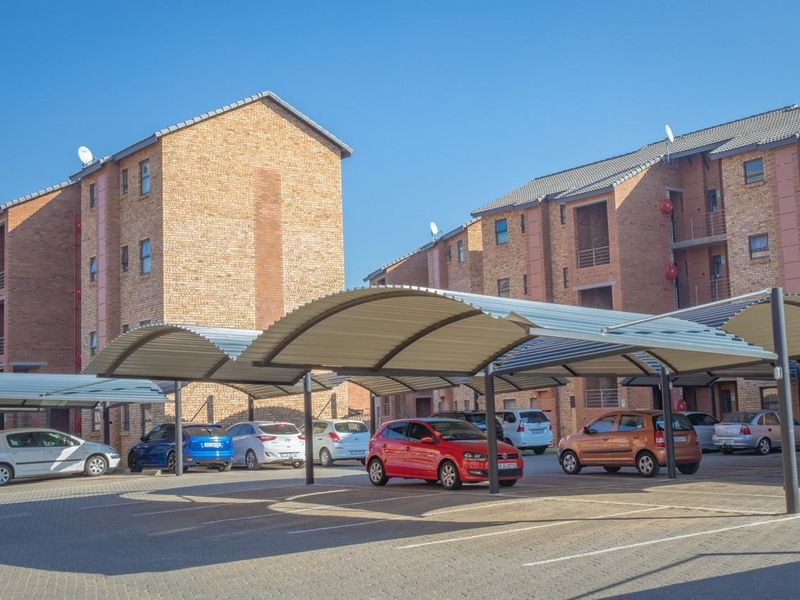Exterior view of an apartment complex featuring paved parking area with covered carports and multi-story brick residential buildings.
