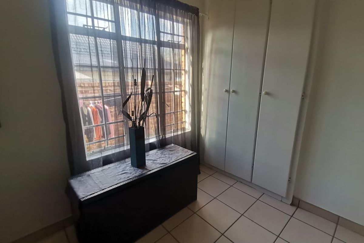 A bedroom featuring tiled flooring, built-in cupboards, and a window fitted with security bars.