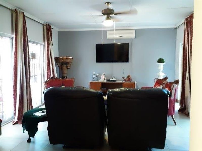 A comfortable living room featuring a ceiling fan, wall-mounted air conditioning unit, and large sliding glass doors providing natural light.