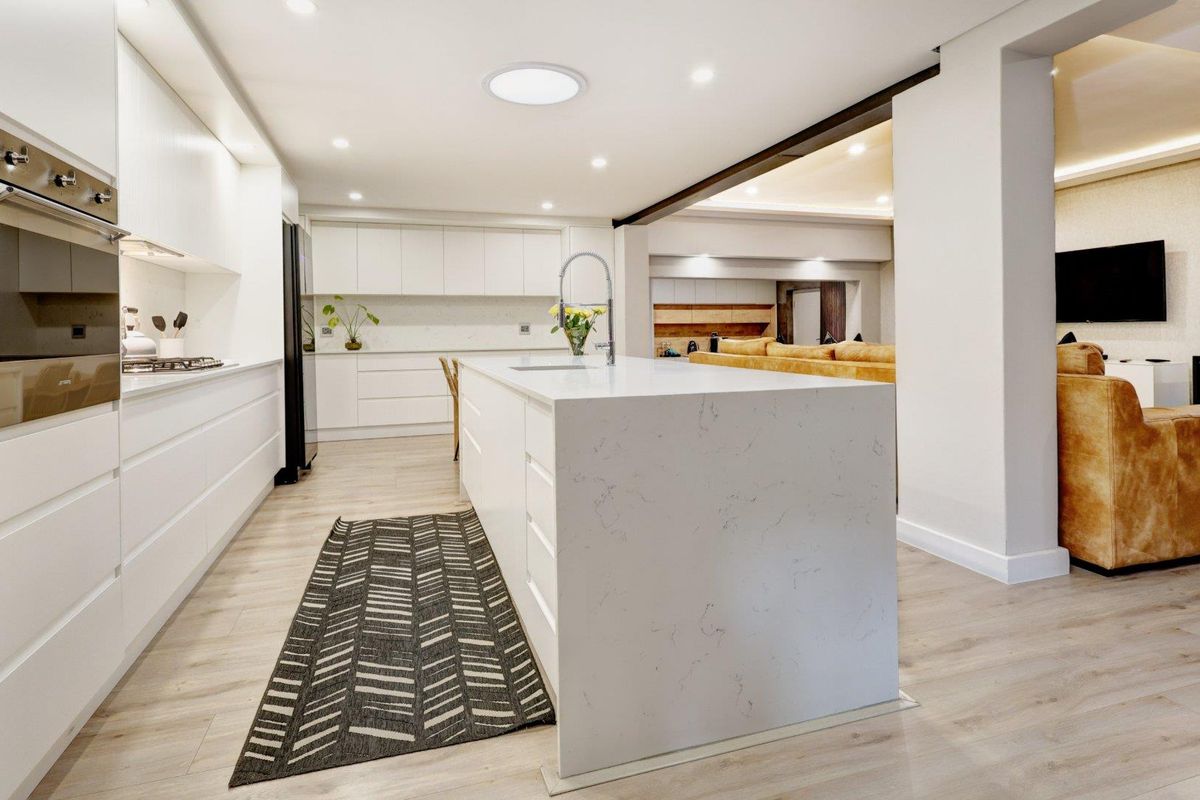 Modern, open-plan kitchen featuring a large stone-topped island, integrated appliances, sleek white cabinetry, and recessed lighting, seamlessly flowing into the adjacent living area.