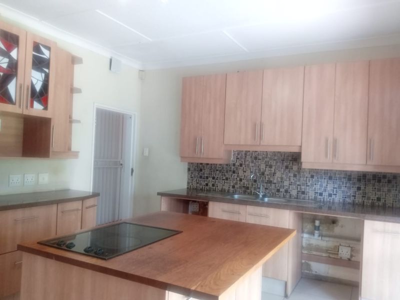 A kitchen featuring light wood cabinetry, a mosaic tile backsplash, and a central island with an integrated hob, requiring minor repairs to cabinetry and finishes.