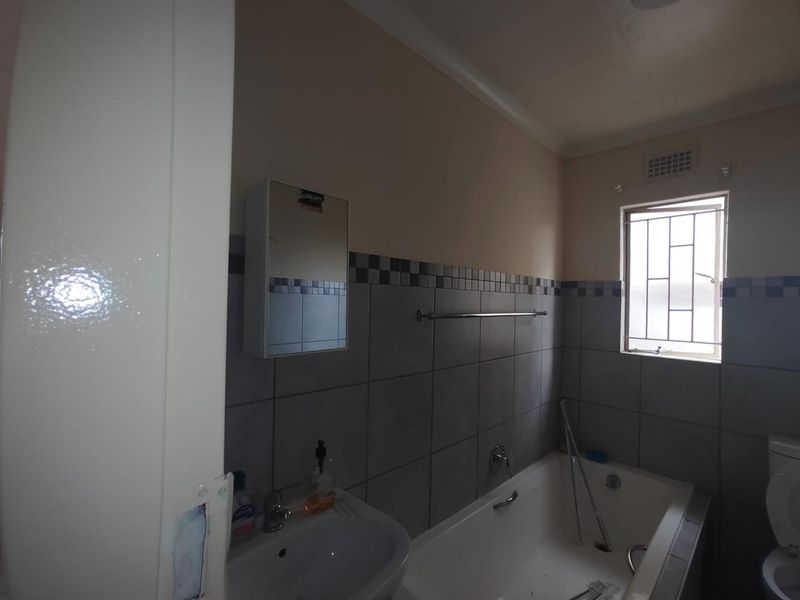 A functional bathroom featuring a built-in bathtub, wall-mounted basin, and tiled splashback, with security bars installed on the window.