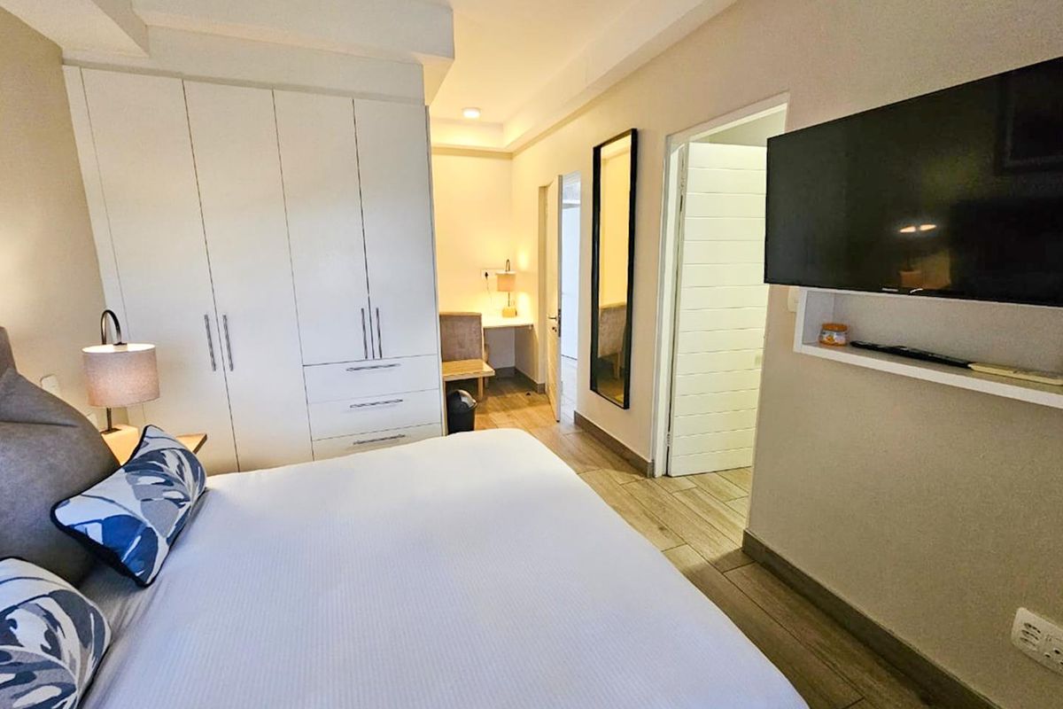 A well-maintained bedroom featuring built-in cupboards, tiled flooring, and a wall-mounted shelf for media storage.