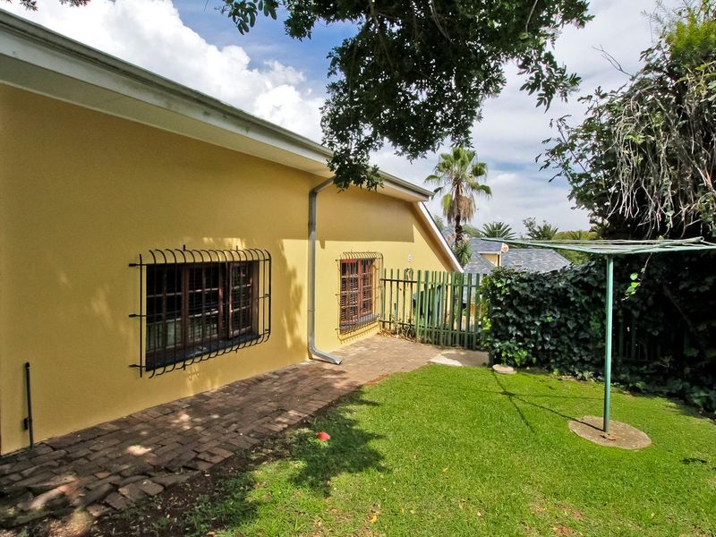 Rear exterior view of the house featuring a brick paved walkway, lawn area, and security-fitted timber windows.