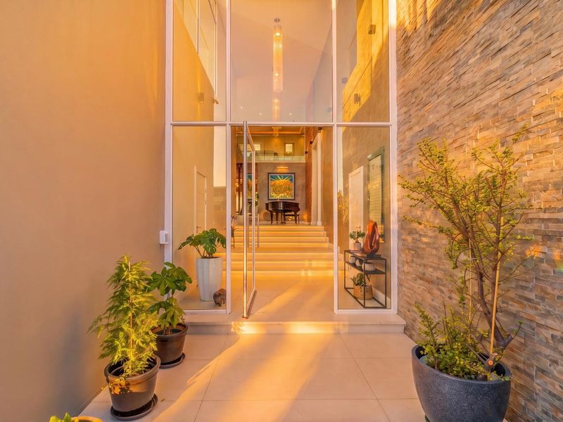 A striking modern entrance featuring a full-height glass pivot door, stacked stone wall cladding, and elegant recessed lighting, creating a warm and inviting arrival.